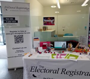 Picture representing our stall with posters, leaflets and information on table. Alongside is our pop up banner with our details and how to register to vote.