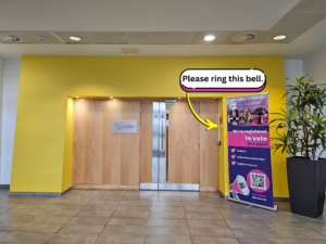 Picture of light brown door and entrance surrounded by yellow walls. Pop up information banner to the right and it shows where the door bell is, which is on the wall on the right hand side if facing the door.